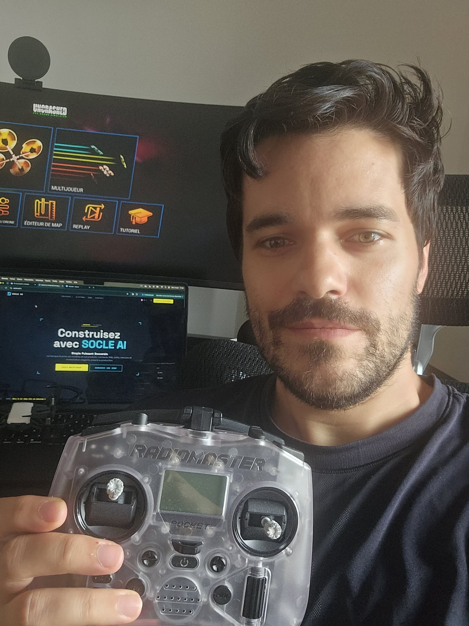 L'auteur tenant une radiocommande RadioMaster Pocket devant un écran affichant le simulateur de drone FPV Uncrashed